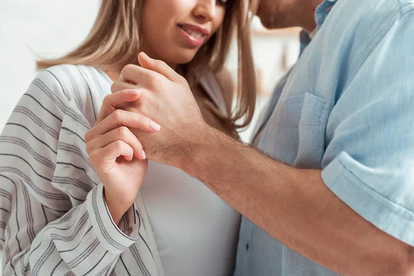 Vista recortada del hombre y la mujer feliz tomados de la mano en casa - foto de stock