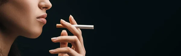Vista lateral de la mujer sosteniendo el cigarrillo aislado en negro, plano panorámico - foto de stock