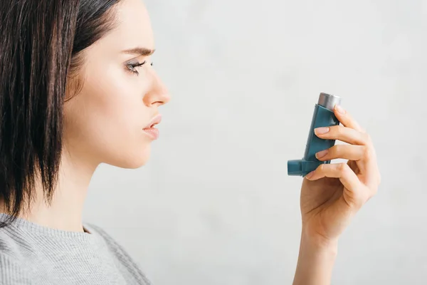 Vista lateral de la mujer joven sosteniendo inhalador sobre fondo blanco - foto de stock