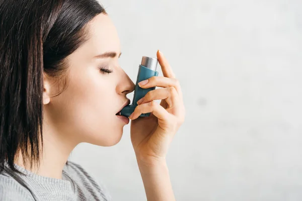 Vista lateral de chica atractiva usando inhalador asmático sobre fondo blanco - foto de stock