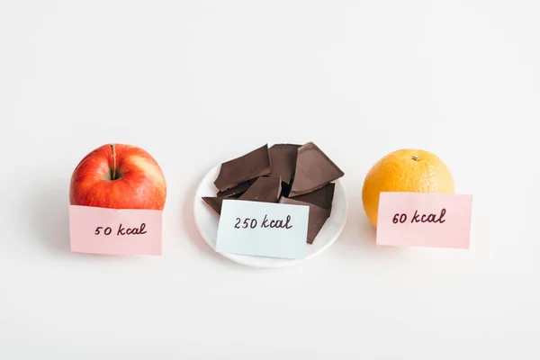 Свежие яблоко, апельсин и шоколад с калориями на карточках на белом фоне, диета подсчета калорий — стоковое фото