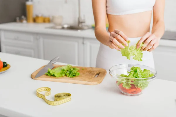 Abgeschnittene Ansicht eines fitten Mädchens, das frischen Salat mit Avocado in der Nähe von Maßband auf dem Küchentisch zubereitet — Stockfoto