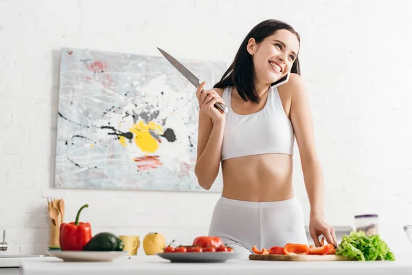 Sportswoman sorrindo falando no smartphone enquanto cozinha salada na mesa da cozinha — Fotografia de Stock