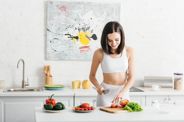 Ensalada de cocina deportiva sonriente con verduras maduras en la mesa de la cocina - foto de stock