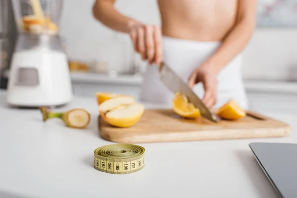 Concentration sélective du ruban à mesurer et des balances près de la fille en forme coupant des légumes frais pour smoothie sur la table de cuisine, régime de comptage des calories — Photo de stock