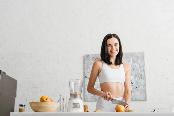 Low angle view of fit sportswoman smiling at camera while preparing smoothie in kitchen — Stock Photo
