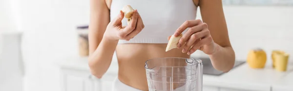 Cropped view of sportswoman putting banana in blender, panoramic shot — Stock Photo