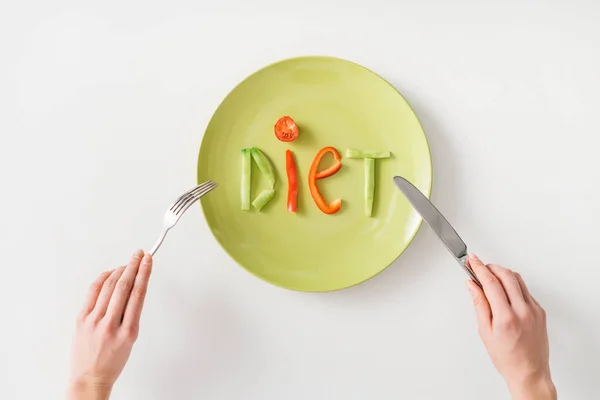 Top view of woman with cutlery near word diet from vegetable slices on plate on white background — Stock Photo