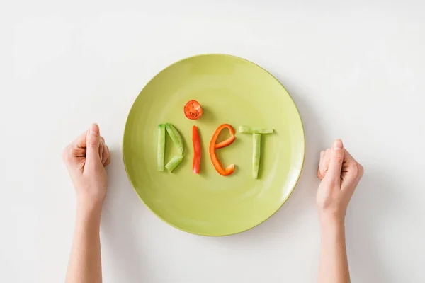 Top view of female fists near word diet from vegetable slices on plate on white background — Stock Photo