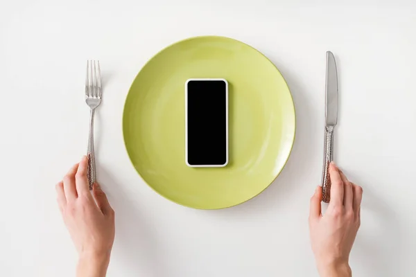 Top view of female hands with cutlery and smartphone on plate on white background — Stock Photo