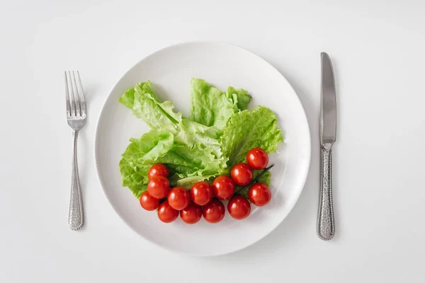 Вид зверху на свіжі овочі на тарілці з столовими приборами на білому тлі — стокове фото