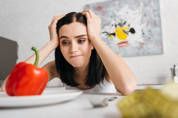 Selective focus of pensive woman looking at bell pepper near measuring tape on table — Stock Photo