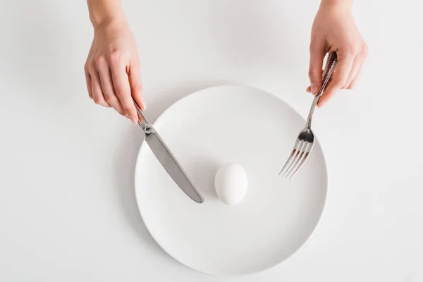 Vista dall'alto della donna che tiene le posate vicino all'uovo sul piatto su sfondo bianco — Foto stock