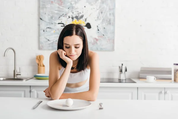 Femme sportive pensive regardant oeuf sur la table de cuisine — Photo de stock