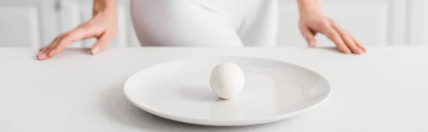 Selective focus of egg on plate and girl near kitchen table, panoramic shot — Stock Photo