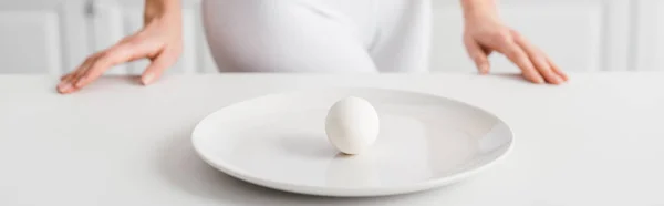 Concentration sélective de l'oeuf sur la plaque et la fille près de la table de cuisine, plan panoramique — Photo de stock