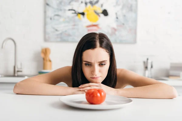 Ragazza pensierosa guardando il pomodoro maturo sul tavolo della cucina — Foto stock