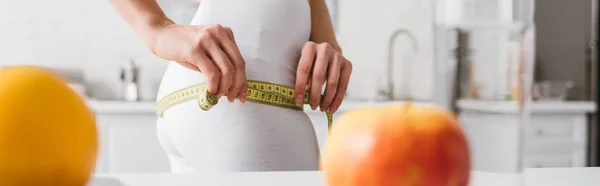 Colpo panoramico di donna in forma che misura i fianchi vicino alla frutta fresca sul tavolo da cucina — Foto stock