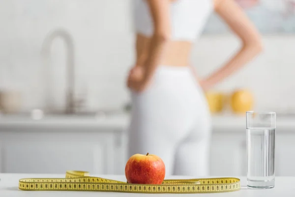 Concentration sélective de pomme, ruban à mesurer et verre d'eau près sportif ajustement dans la cuisine — Photo de stock