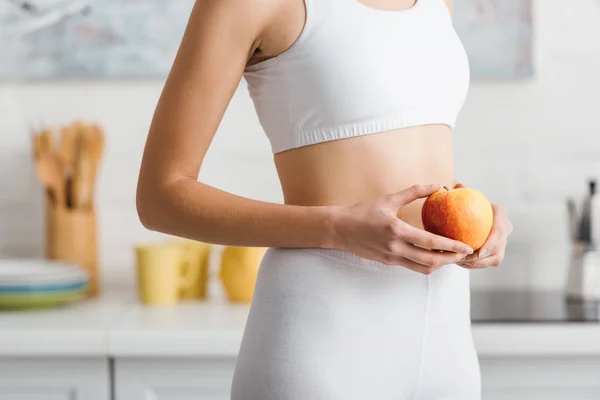 Cropped view of fit sportswoman holding fresh apple in kitchen — Stock Photo