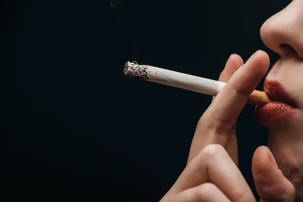 Vista lateral de la mujer fumando cigarrillo aislado en negro - foto de stock