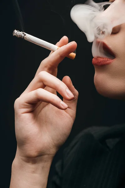 Vista recortada de la mujer fumando cigarrillo aislado en negro - foto de stock