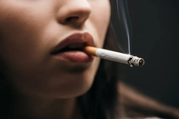 Enfoque selectivo de la mujer joven fumando cigarrillo aislado en negro - foto de stock