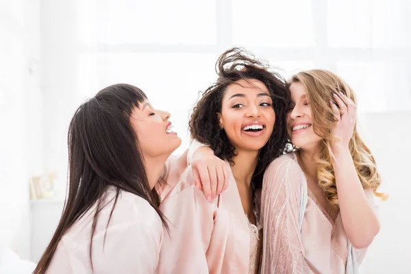 Heureux multiculturels filles en peignoirs câlins sur enterrement de vie de jeune fille — Photo de stock