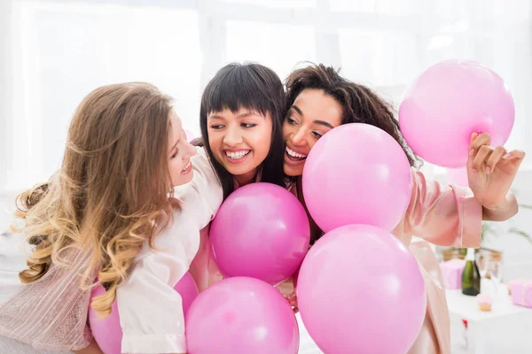 Emotional multicultural girls having fun with pink balloons on pajama party — Stock Photo