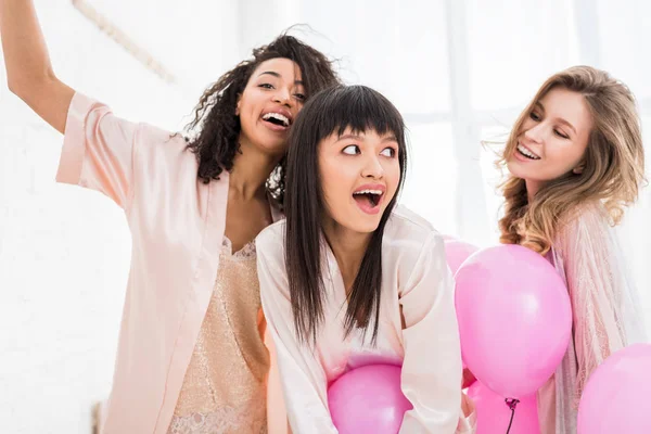 Excité filles multiculturelles ayant enterrement de vie de jeune fille avec des ballons roses — Photo de stock