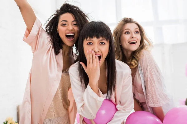 Chicas multiétnicas emocionadas divirtiéndose con globos rosados en el dormitorio - foto de stock