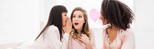 Plan panoramique de copines multiculturelles choquées chuchotant et bavardant sur la fête de célibataire — Photo de stock