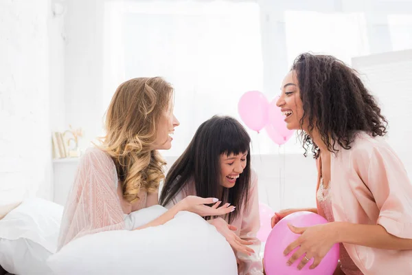 Felizes namoradas multiculturais rindo na cama com balões rosa — Fotografia de Stock