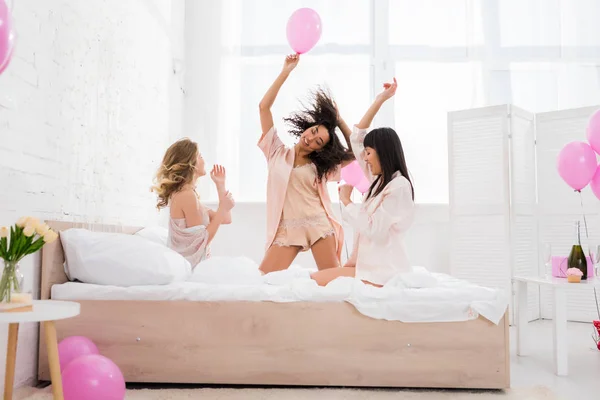 Счастливые мультикультурные девушки веселятся и танцуют с розовыми шариками в спальне — стоковое фото