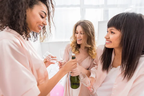 Sorrindo meninas multiétnicas abrindo garrafa de champanhe na despedida de solteira — Fotografia de Stock