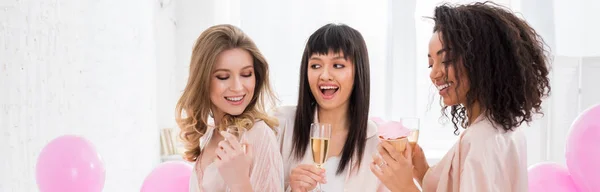 Plano panorámico de chicas multiétnicas divirtiéndose con champán y magdalena durante despedida de soltera con globos rosados - foto de stock
