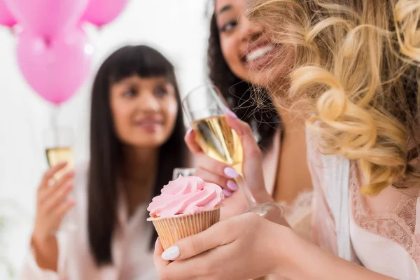Foco seletivo de namoradas multiculturais felizes se divertindo com champanhe e cupcake durante a festa de despedida de solteira — Fotografia de Stock
