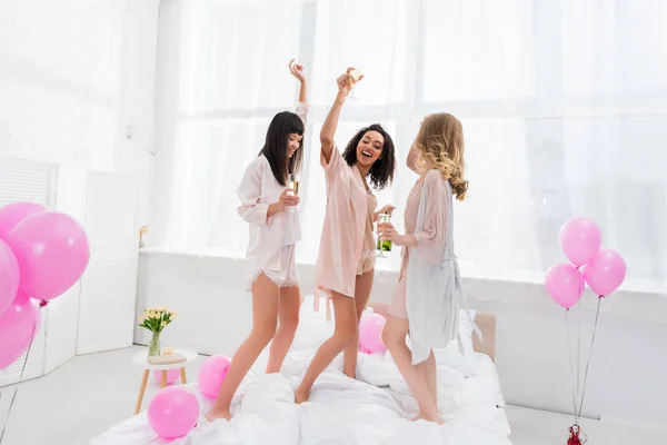 Cheerful multiethnic girls dancing with champagne glasses on bachelorette party with balloons — Stock Photo