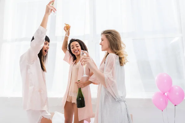 Filles multiculturelles émotionnelles dansant avec des verres de champagne sur enterrement de vie de jeune fille avec des ballons — Photo de stock