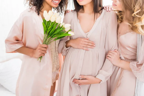 Vista recortada de la mujer embarazada joven con amigas y flores de tulipán en la ducha de bebé - foto de stock