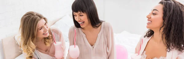 Panoramic shot of multicultural girlfriends and laughing pregnant woman holding glasses with milkshakes on baby shower — Stock Photo