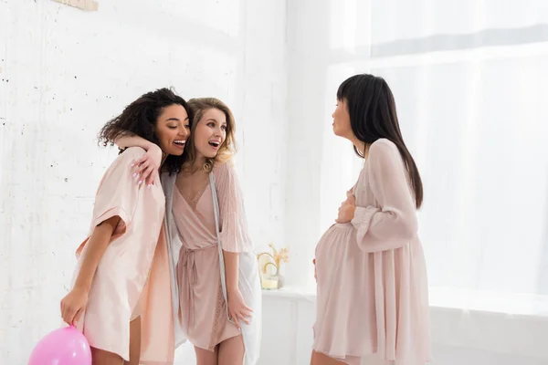 Мультикультурні подружки з рожевою кулею дивляться на молоду вагітну жінку на дитячому душі — стокове фото
