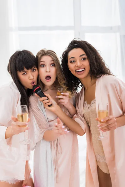 Красиві збуджені мультикультурні дівчата тримають шампанське і співають з мікрофоном на дівич-вечір — Stock Photo
