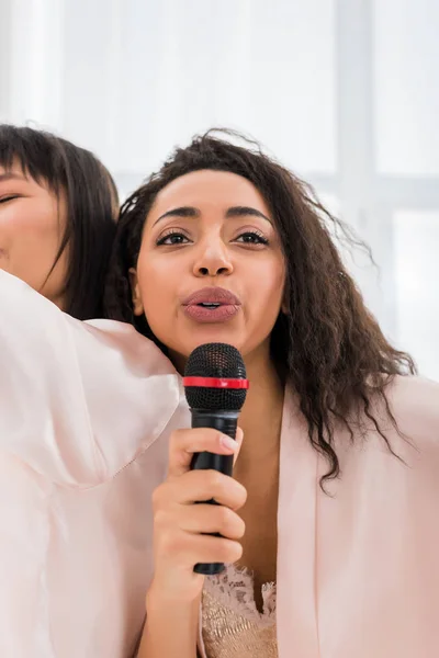 Multicultural girlfriends singing with microphone on pajama party — Stock Photo