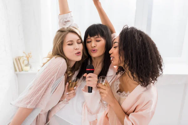Beautiful happy multicultural girls singing with microphone on pajama party — Stock Photo