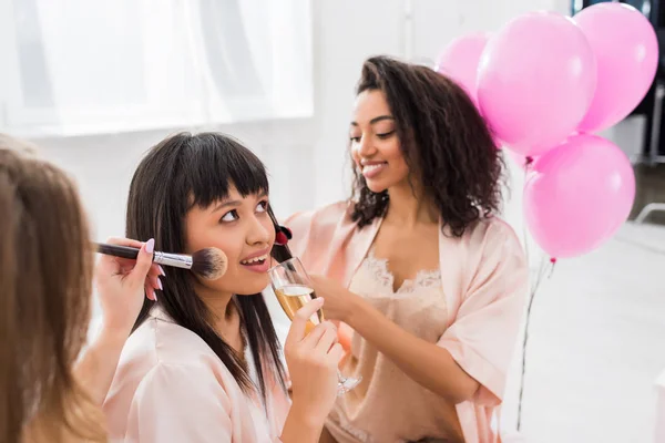 Filles multiethniques faisant coiffure, maquillage et boire du champagne sur la fête de célibataire — Photo de stock