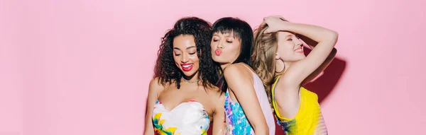 Panoramic shot of happy fashionable multicultural girlfriends dancing on pink — Stock Photo