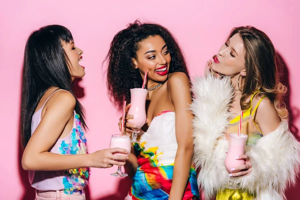 Happy stylish multiethnic girls drinking milkshakes on pink — Stock Photo