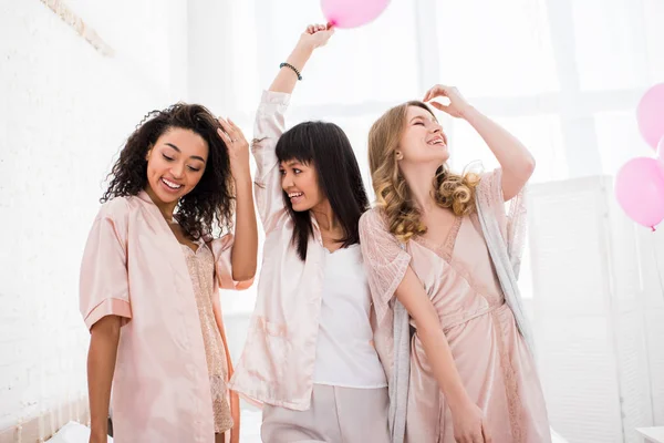 Smiling multicultural girls having fun in bedroom with pink balloons for party — Stock Photo