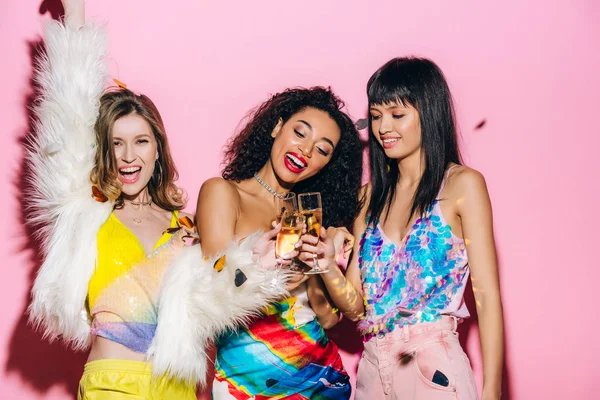 Joyeuses filles multiculturelles s'amuser avec des verres de champagne sur rose avec des confettis — Photo de stock